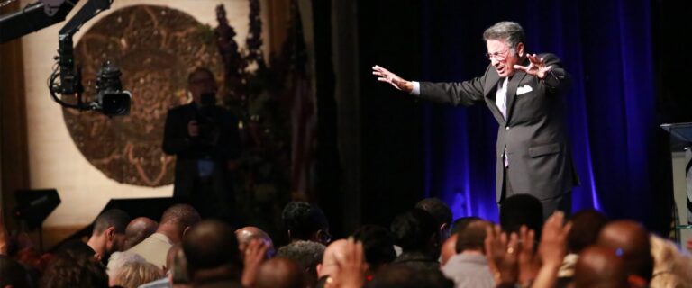 Dr. Youssef prays with hands outstretched over a congregation