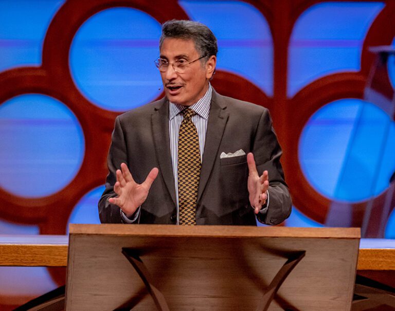 Dr. Youssef smiling and talking at a colorful podium onstage