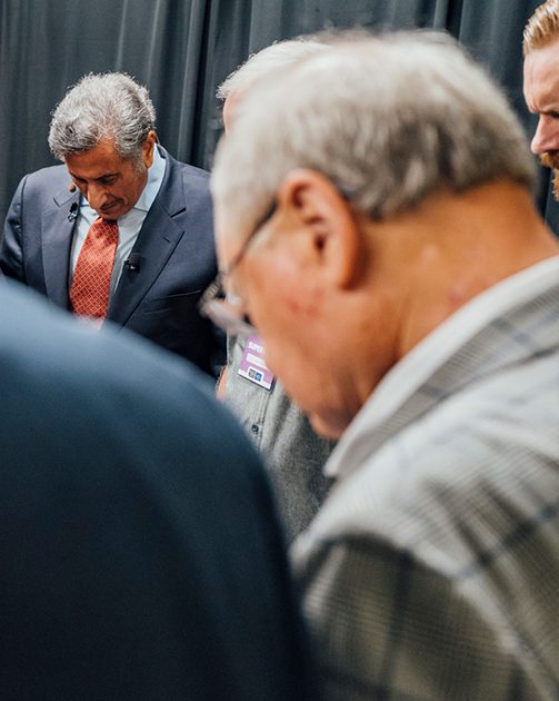 close up image of men in a group praying with their heads bowed